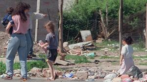 Mujer y niños caminando por una calle con escombros, imagen de la nota "Claves para entender cuando se habla de hambre y niñez en la Argentina".