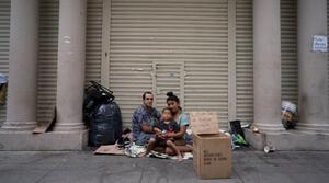 Familia sentada en la vereda con pertenencias y un cartel pidiendo ayuda, imagen de la nota "Infancias en riesgo: más de la mitad de los chicos es pobre y 316 mil están en situación de vulnerabilidad extrema en la Argentina".