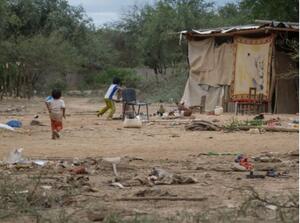 Dos niños corren por un terreno de tierra con basura esparcida, cerca de una vivienda precaria, imagen de la nota "La deuda que más duele | Duro informe sobre la desnutrición infantil en Salta".