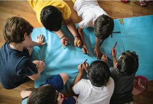 Captura de imagen de la nota "Presentan un amparo contra el Congreso para que la Defensoría de la niñez no quede acéfala". En la foto, un grupo de niños dibuja sobre un papel grande en el piso, visto desde arriba.